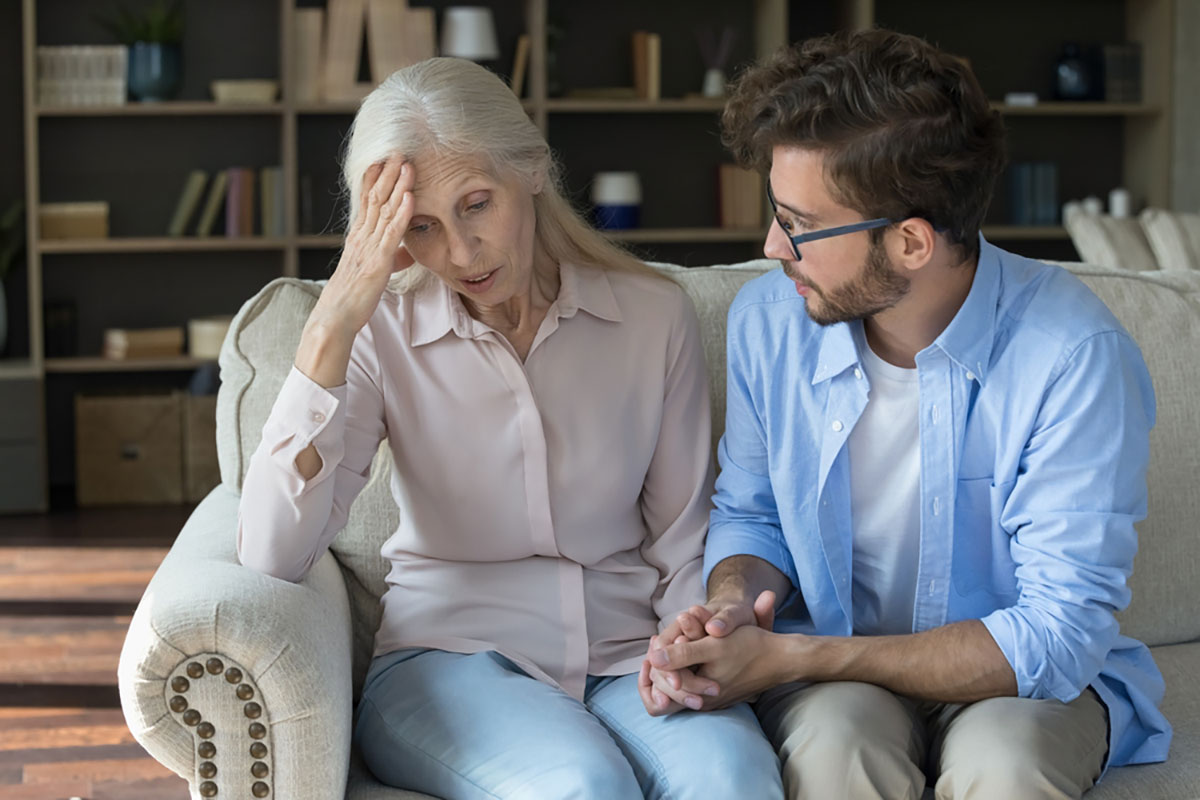 An older woman looking worried as a younger man sits beside her, holding her hand in support.